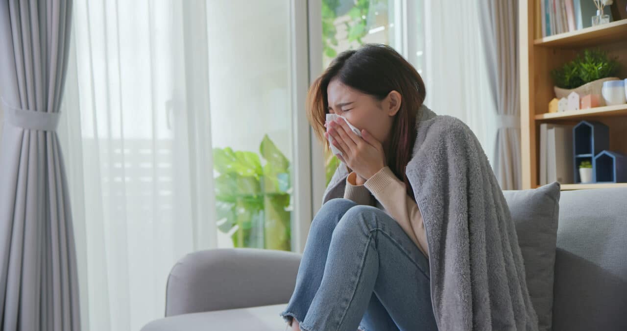 Woman holding her nose with a tissue while sitting on a couch.