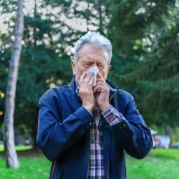 a man with allergies blows his nose outside
