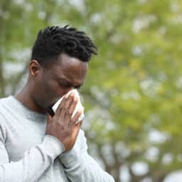 Man with allergies blowing his nose outdoors.