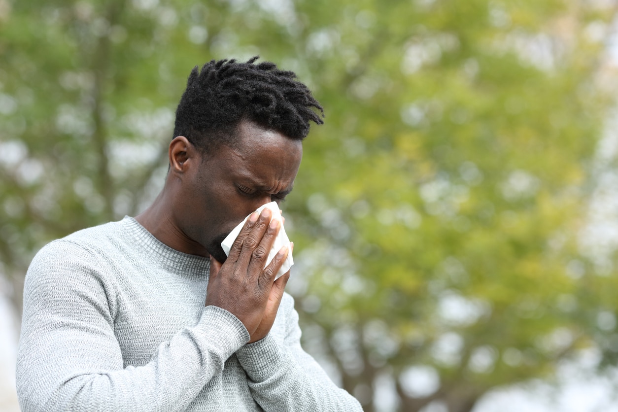 Man with allergies blowing his nose outdoors.
