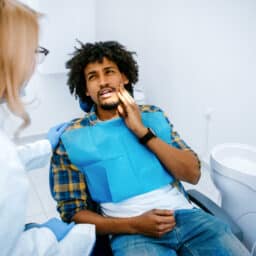 Man holding his jaw telling dentist about tooth pain