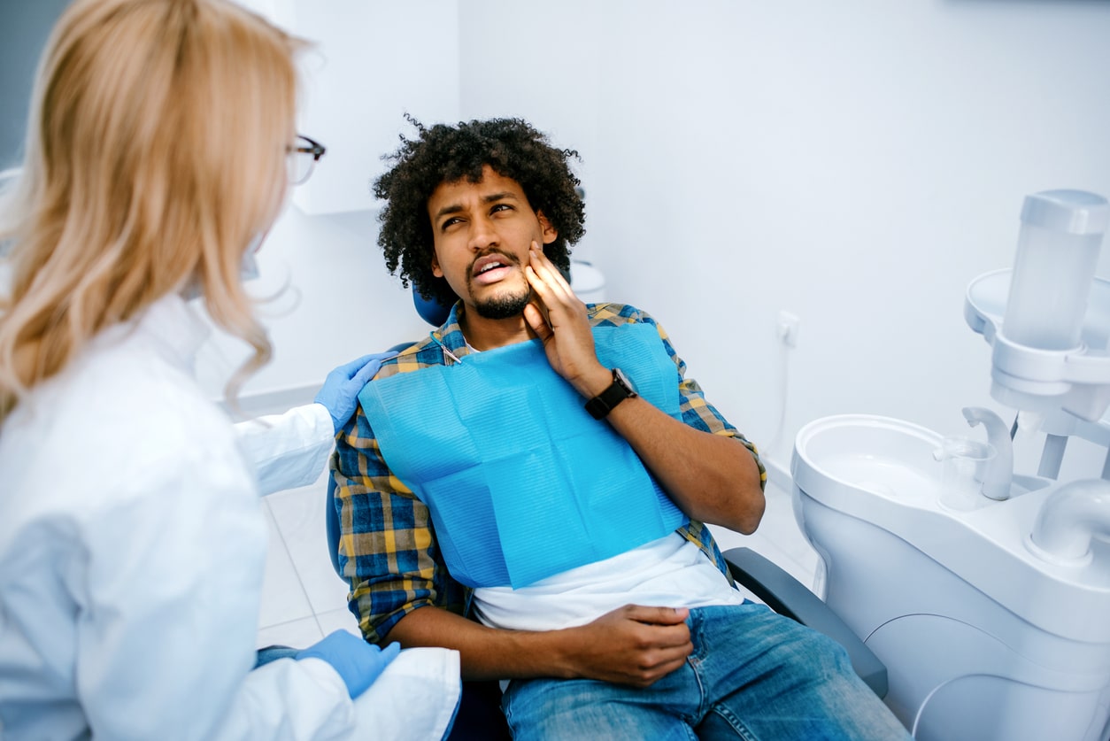 Man holding his jaw telling dentist about tooth pain.