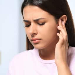 Young woman holding her ear with tinnitus