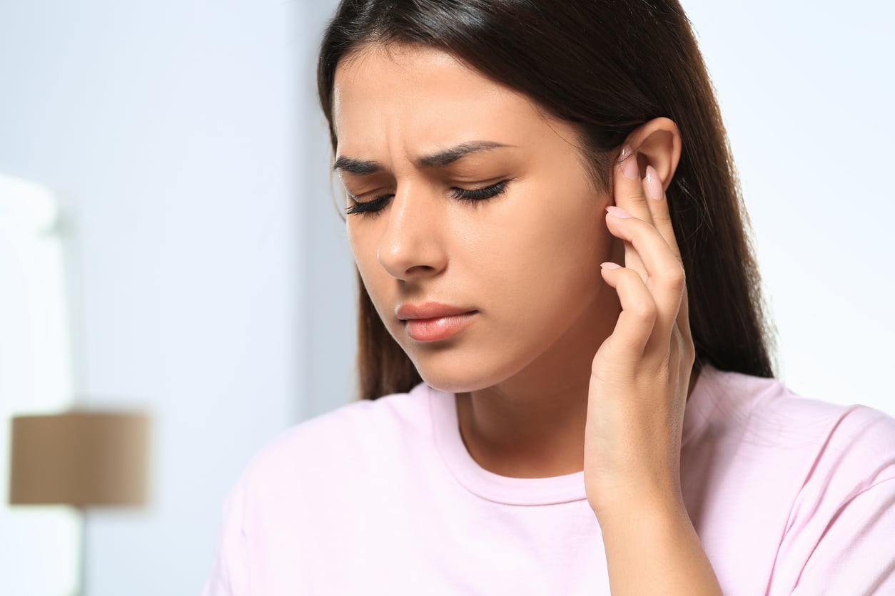 Young woman holding her ear with tinnitus