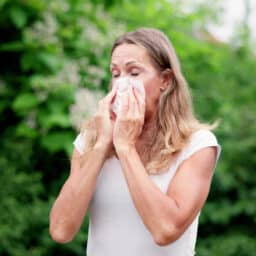 Woman with allergies blowing her nose outside.