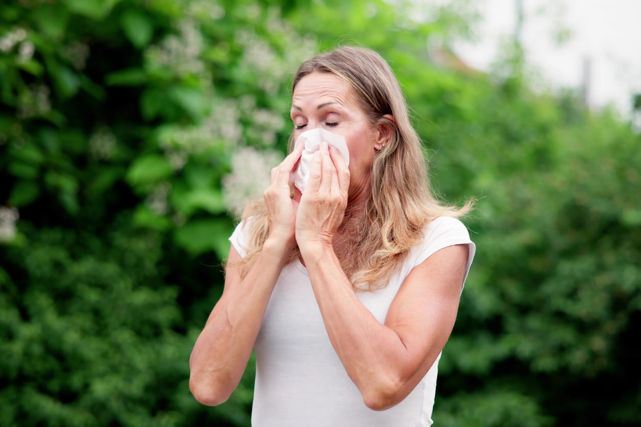 Woman with allergies blowing her nose outside.