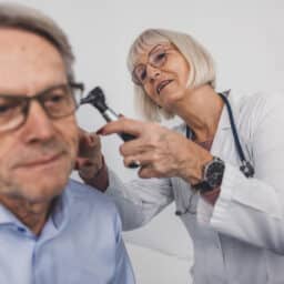 Audiologist examining patient's ear with otoscope