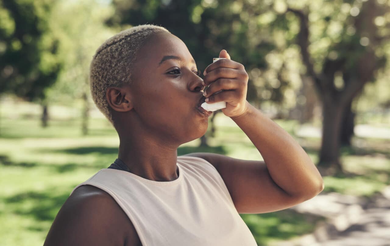 Woman using her asthma inhaler at the park