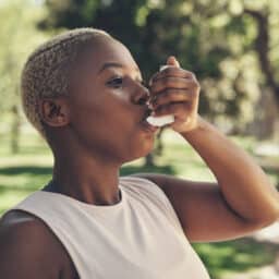 Woman using her asthma inhaler at the park