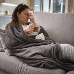 Woman resting on sofa drinking hot tea and massaging her nose
